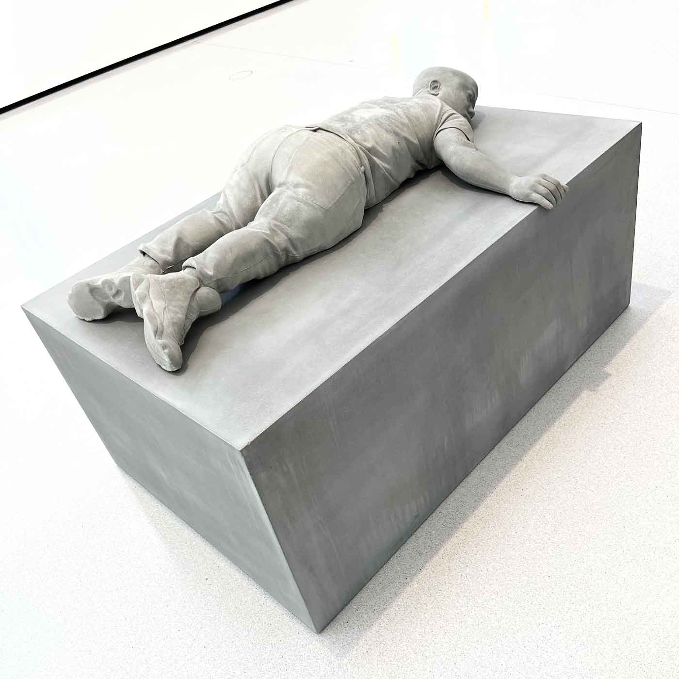 Skulptur eines Zwergs in Sneaker liegend auf einem Quader
