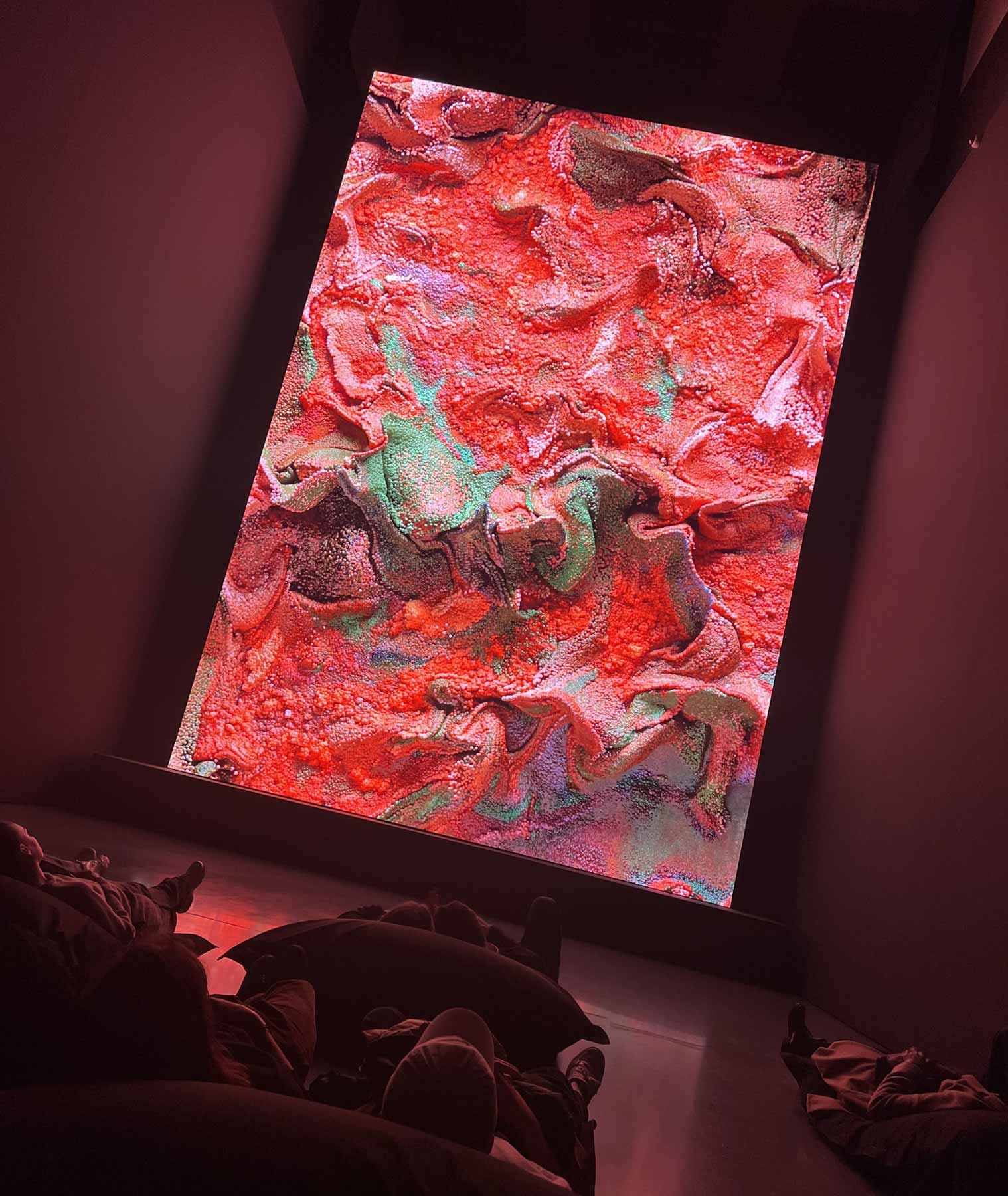 Museumsbesucher liegen vor einer riesigen LED-Wand mit abstrakten Pixelwelten