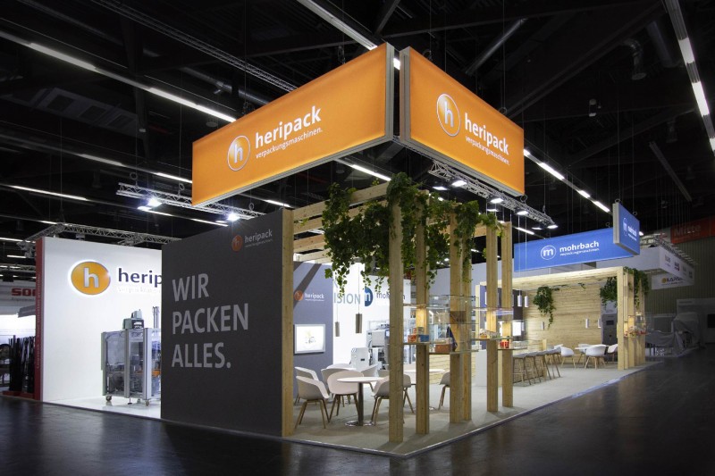 Messestand für Mohrbach auf der Fachpack, Nürnberg 2019, Glasvitrinen, Holzstruktur, Lounge, Bar, Leuchtlogos, Messegrafik, Maschinen